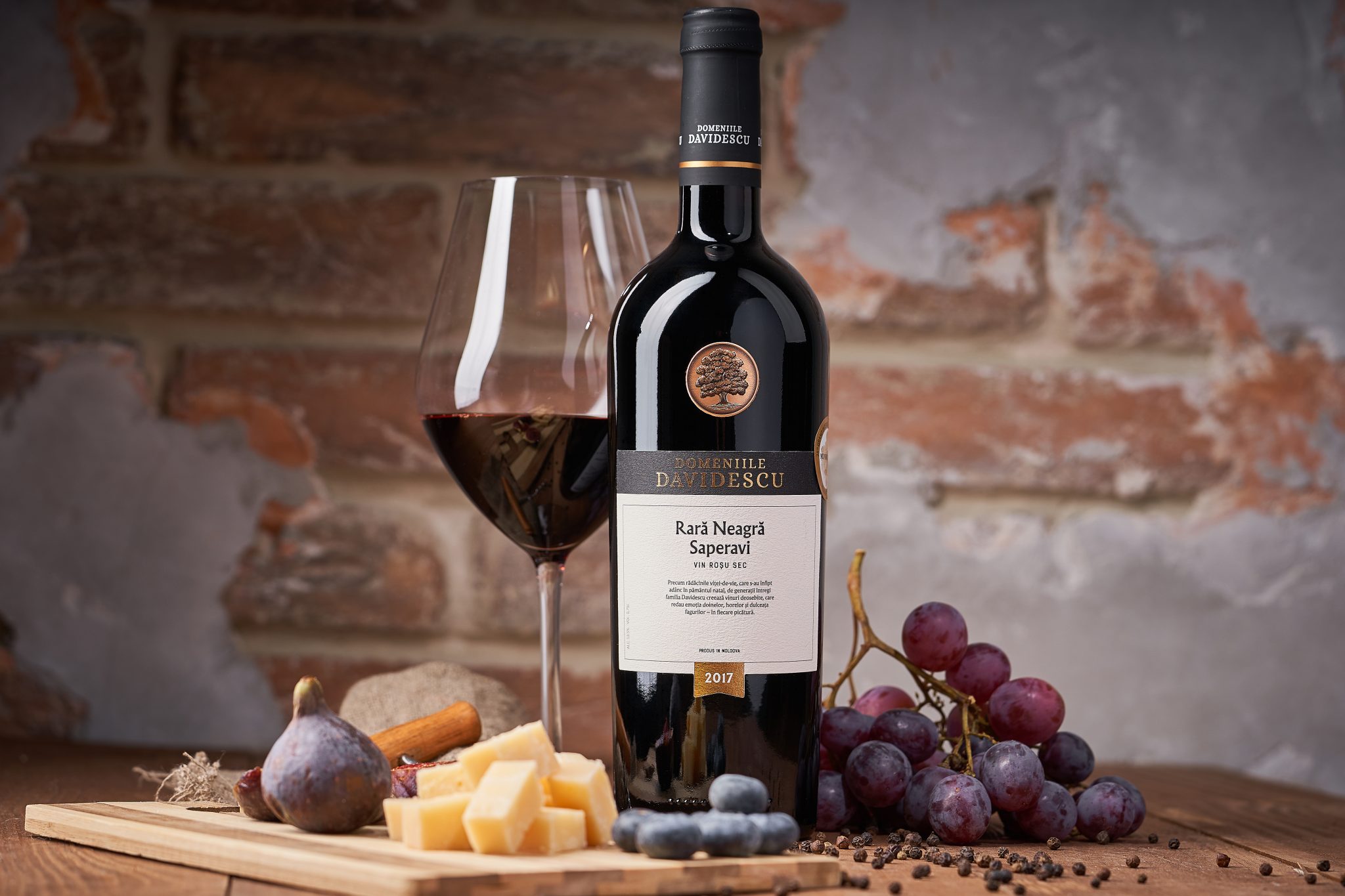 O sticlă de vin roșu de la Domeniile Davidescu, cu un pahar, alaturi de fructe si branzeturi